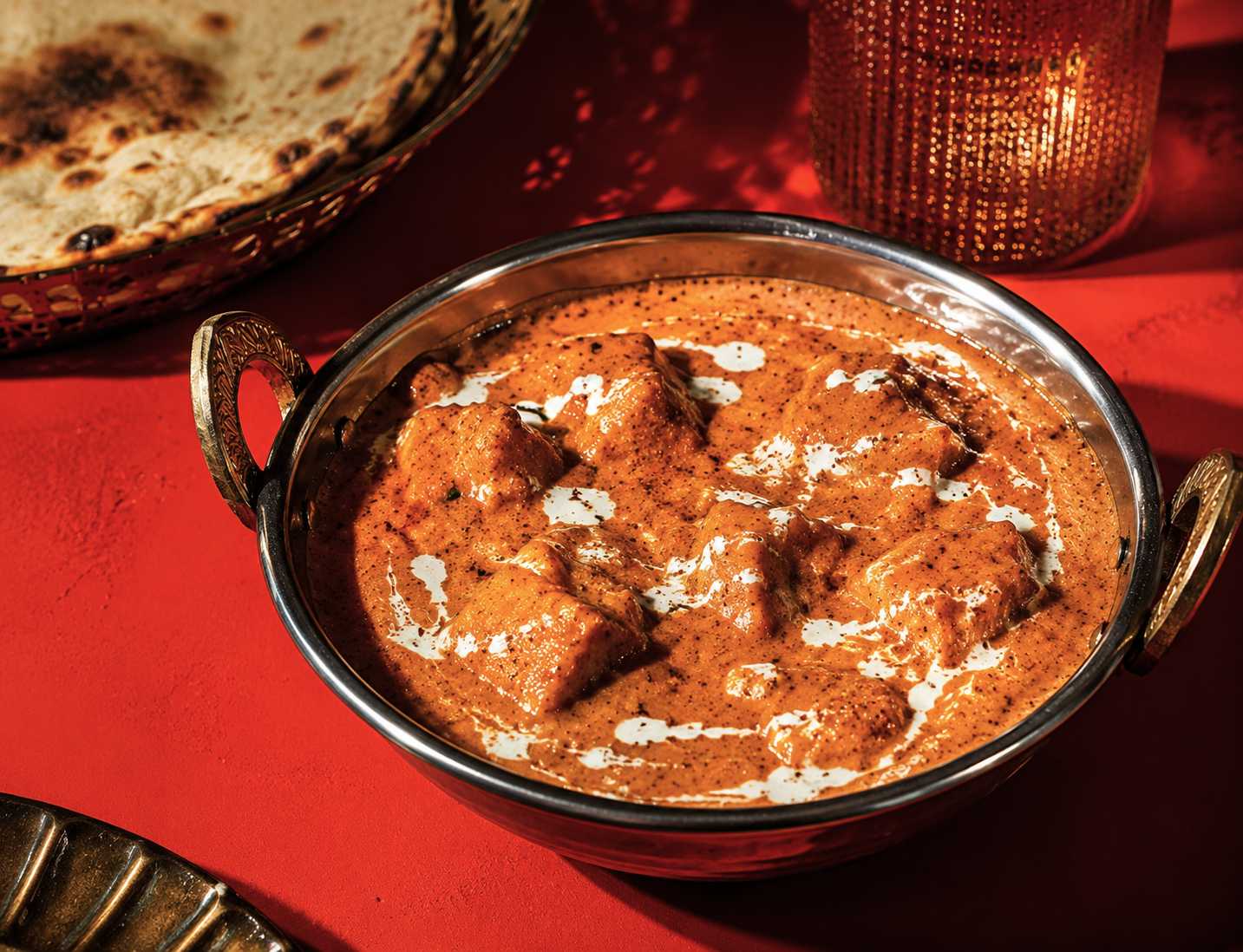 A copper karahi of creamy SIMMR butter masala curry served with charred naan